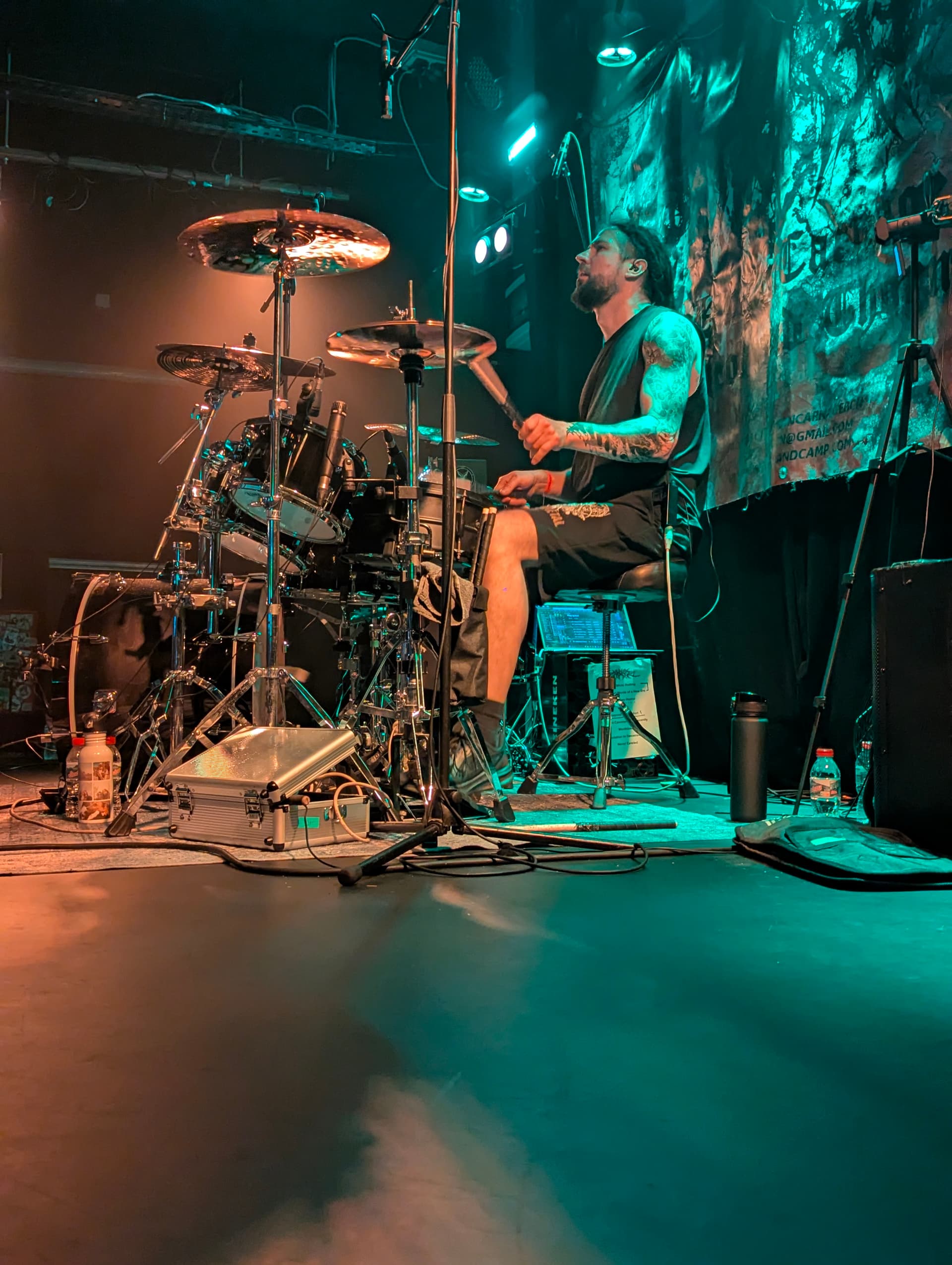 Performing drums in profile under teal stage lighting at a live show